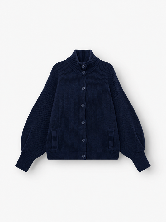 Die Strickjacke „Bomber Dunkelblau“ ist eine marineblaue Damen-Strickjacke mit langen Ärmeln, hohem Kragen, Knopfleiste vorne, gerippter Struktur, zwei Vordertaschen und leicht ausgestellten Ärmeln. Dieses stilvolle Kleidungsstück wird flach auf einem weißen Hintergrund präsentiert.