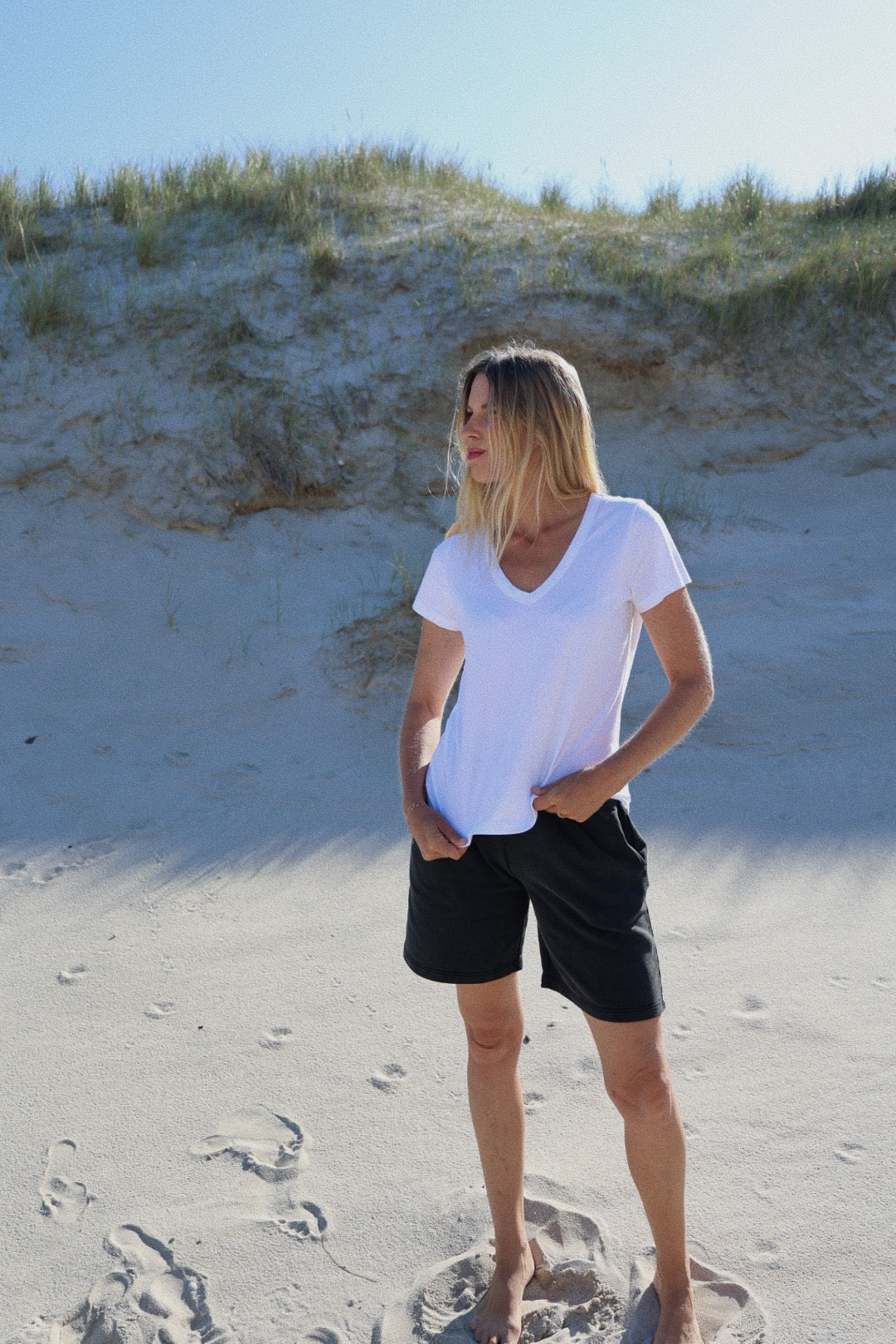 Eine Frau steht im Sand und trägt ein weißes T-Shirt V-Neck aus 100% Baumwolle.