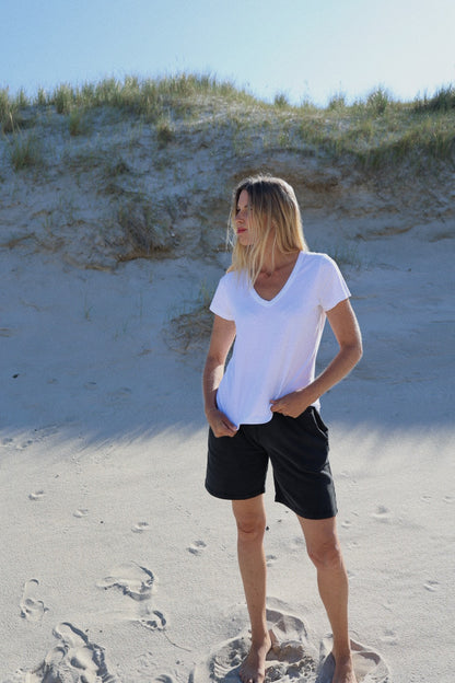 Eine Frau steht im Sand und trägt ein weißes T-Shirt V-Neck aus 100% Baumwolle.