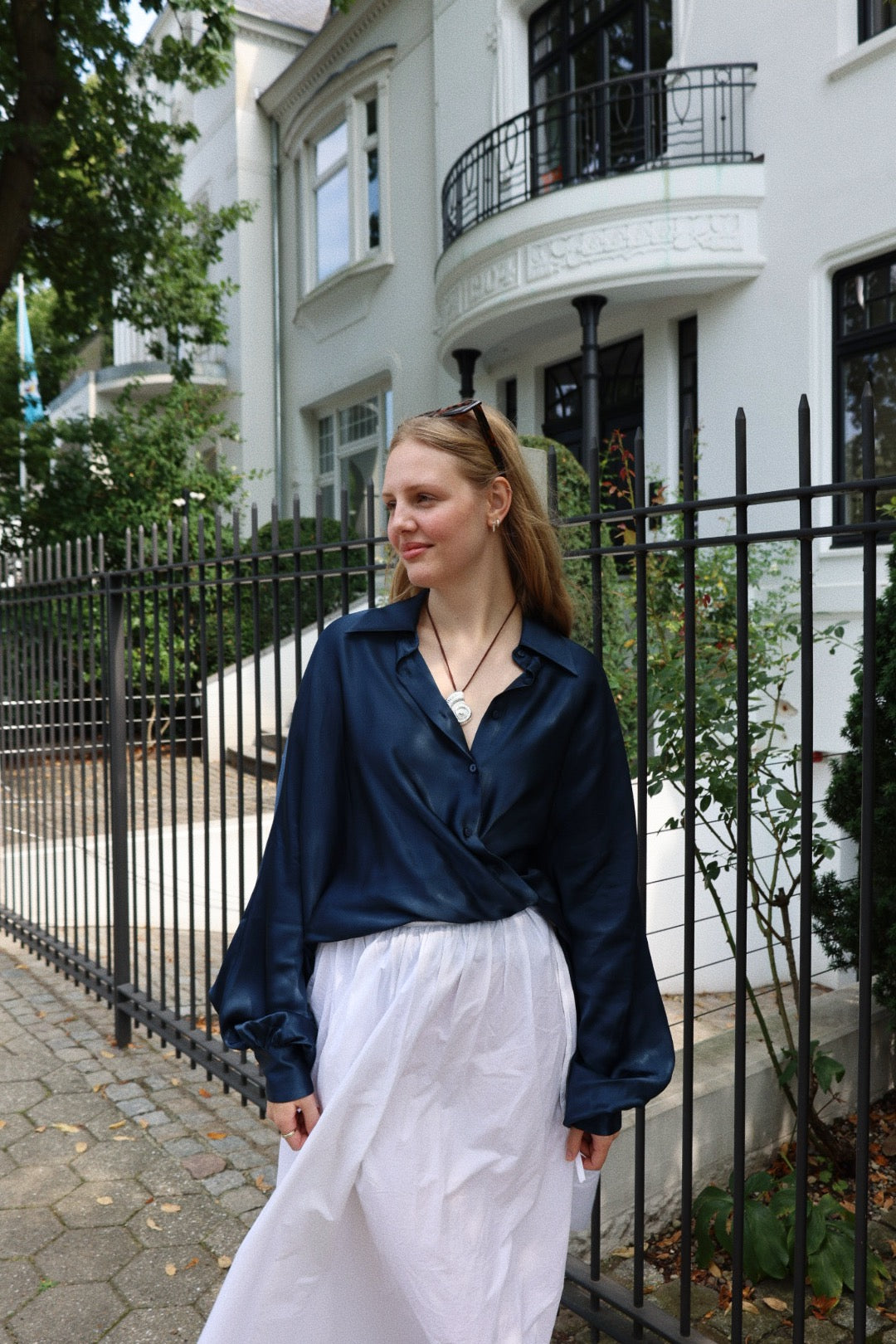 Eine Frau steht an einem Zaun und trägt die Bluse Antonia Shiny Navy aus der Kollektion Antonia Bluse Damen.