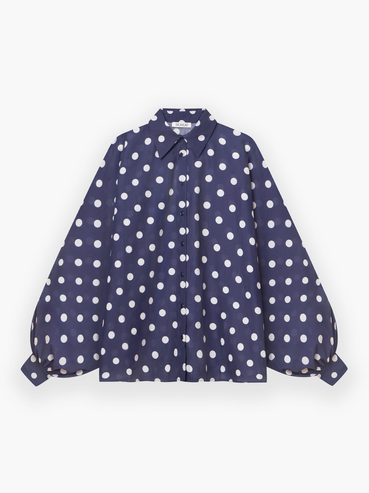 Die Antonia Dots Navy Ecru ist eine marineblaue Bluse in Übergröße aus weichem Baumwollvoile mit ecrufarbenen Punkten, voluminösen langen Ärmeln mit geknöpften Manschetten und einem klassischen Kragen. Hier auf weißem Grund abgebildet.