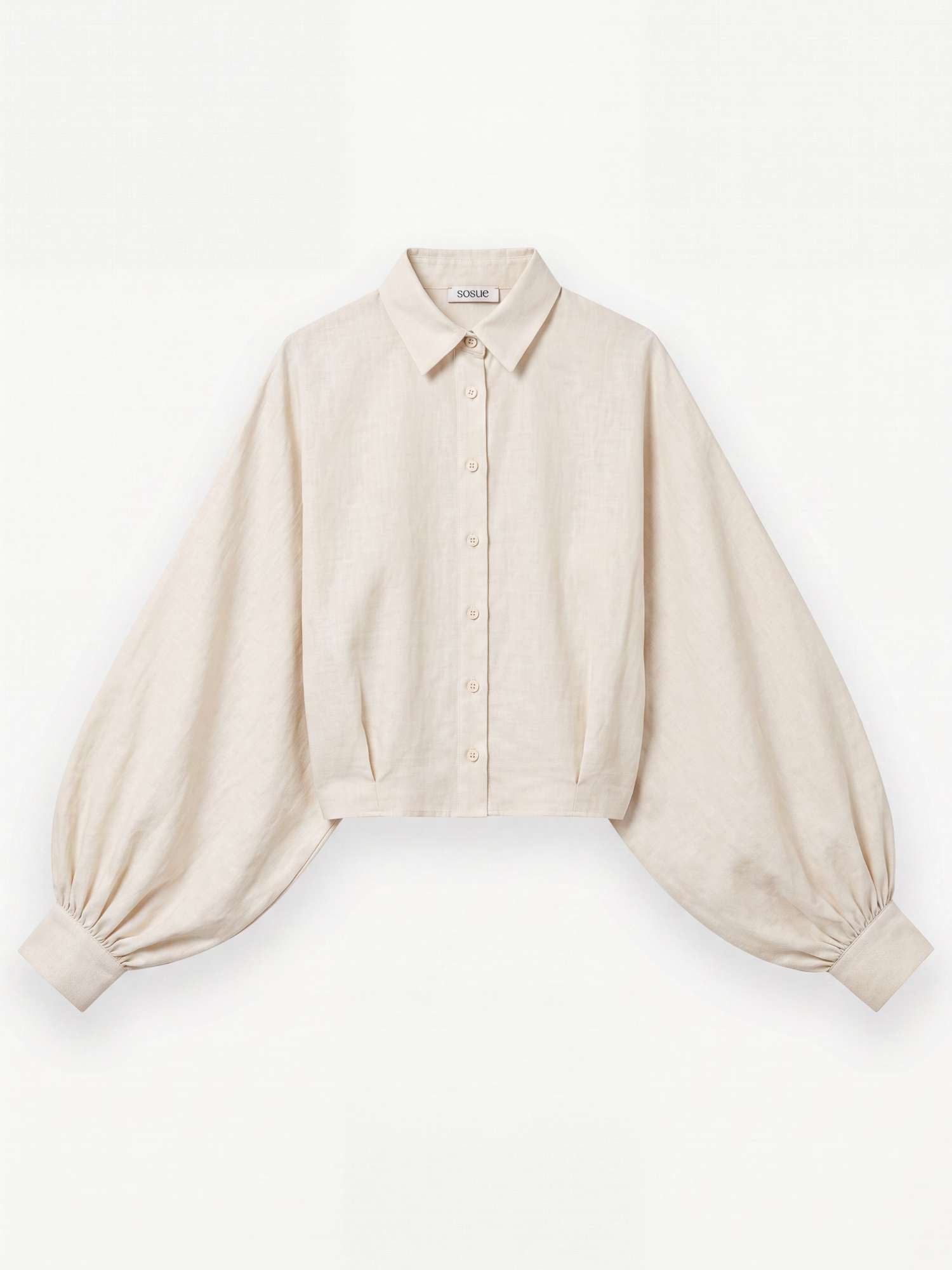 Die Bluse „Antonia Short Flanell Offwhite“ – eine beigefarbene, kurz geschnittene Bluse aus hochwertigem Flanell, hergestellt in Portugal – verfügt über einen Kragen, eine Knopfleiste vorne und auffällige Ballonärmel, die an den Manschetten gerafft sind. Das Kleidungsstück wird flach auf einem weißen Hintergrund präsentiert.