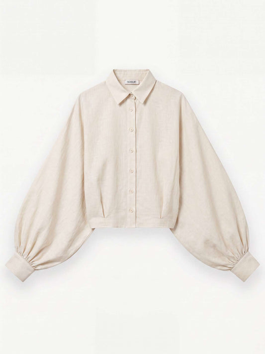 Die Bluse „Antonia Short Flanell Offwhite“ – eine beigefarbene, kurz geschnittene Bluse aus hochwertigem Flanell, hergestellt in Portugal – verfügt über einen Kragen, eine Knopfleiste vorne und auffällige Ballonärmel, die an den Manschetten gerafft sind. Das Kleidungsstück wird flach auf einem weißen Hintergrund präsentiert.