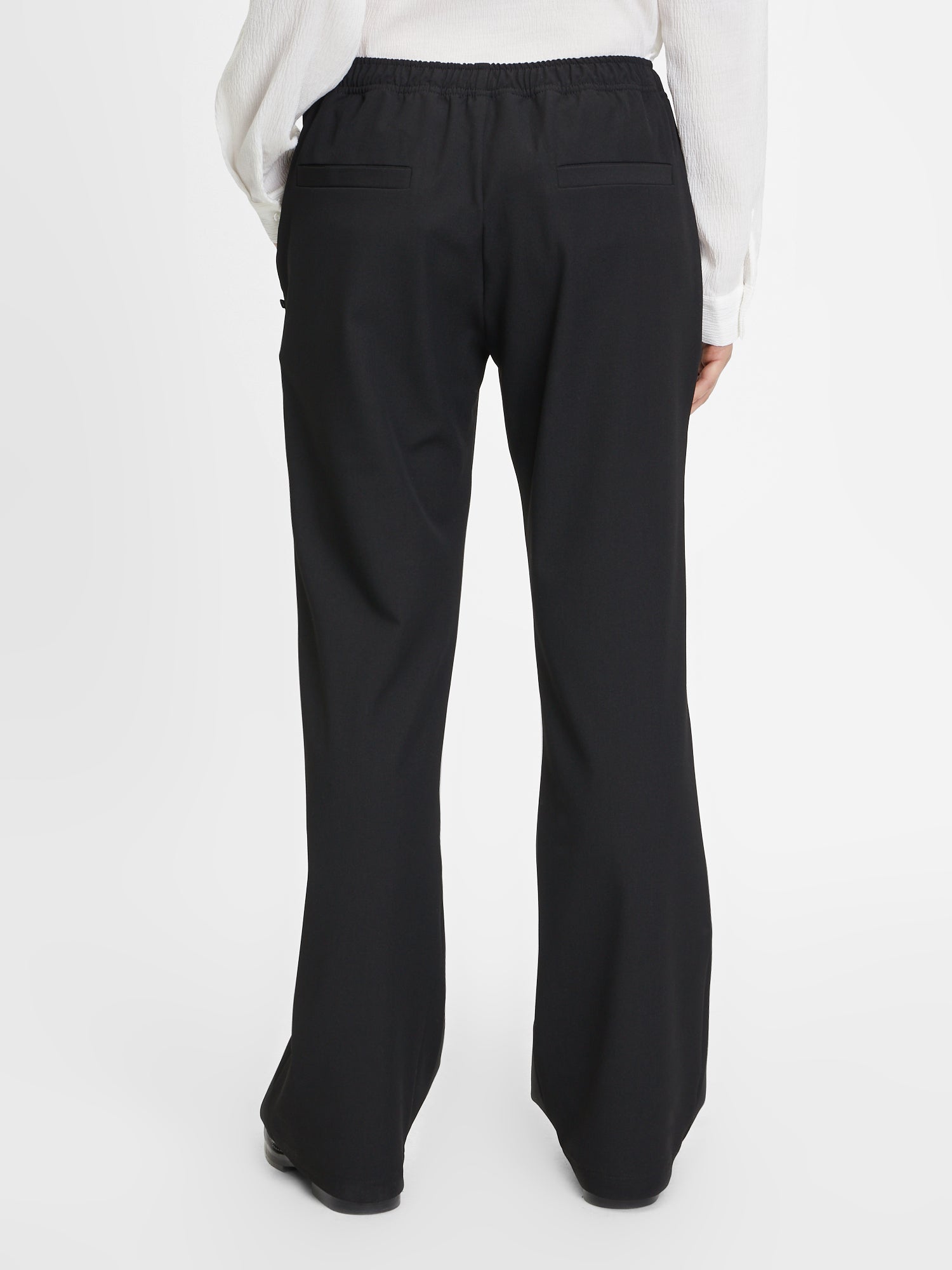 Vor einem schlichten weißen Hintergrund ist eine Person von hinten zu sehen, die ein weißes langärmeliges Hemd mit dem Schriftzug Karoline Black trägt - ideal als Teil eines modernen Business-Outfits für Frauen.