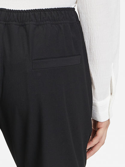 Man sieht eine Person von hinten, die die Hose Karoline Black mit Gummibund und ein weißes langärmeliges Hemd trägt; nur der untere Rücken und eine Hand sind zu sehen.