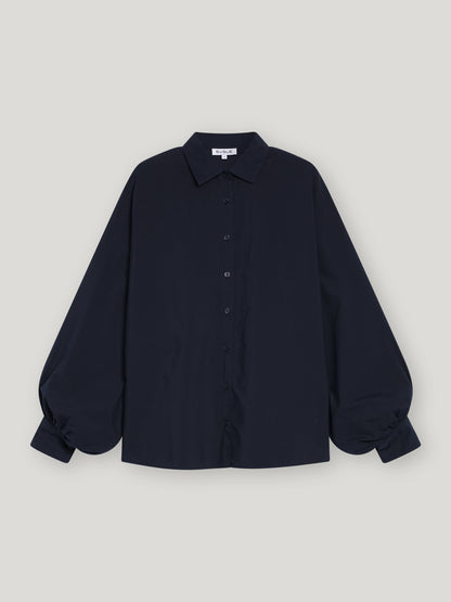 Die Bluse Antonia Slim Dark Blue, eine schmal geschnittene Damenbluse mit langen Ärmeln, Kragen und voluminös gerafften Manschetten, präsentiert sich elegant vor einem schlichten hellgrauen Hintergrund.