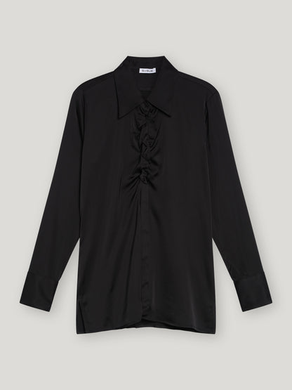Die Bluse Ella Shiny Black ist eine schwarze Satinbluse mit klassischem Kragen, gerafften Details an der Vorderseite und tailliertem Schnitt. Sie ist flach auf einem hellgrauen Hintergrund ausgelegt.