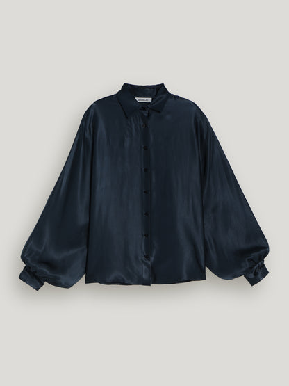 Die Antonia Shiny Navy ist eine langärmelige, dunkelmarinefarbene Satin-Damenbluse mit geknöpfter Vorderseite, Kragen und voluminösen Ballonärmeln für einen eleganten Oversized-Look, abgebildet auf einem hellgrauen Hintergrund.