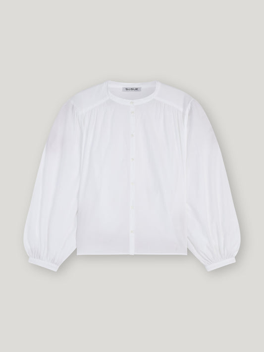 Die Bluse Bella White hat einen Rundhalsausschnitt, eine geknöpfte Vorderseite, geraffte Schultern und Puffärmel mit geknöpften Manschetten in einer übergroßen Silhouette, die sich vor einem hellgrauen Hintergrund präsentiert.