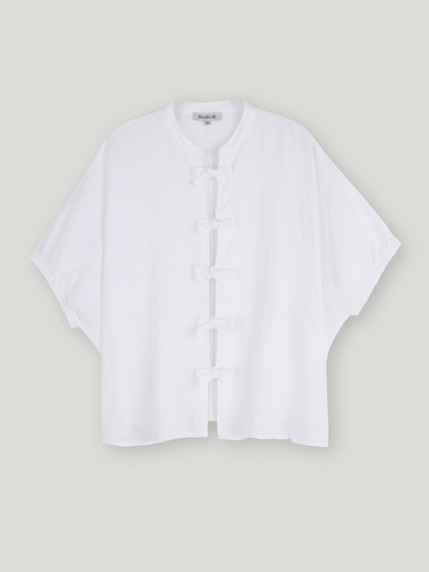 Die Bluse Cowboy Bow ist eine locker sitzende weiße Leinenbluse für Damen mit kurzen Ärmeln, Mandarinkragen und fünf traditionellen Knotenverschlüssen auf der Vorderseite. Auf hellgrauem Grund ist sie die ideale Wahl für Fans der nachhaltigen Mode.