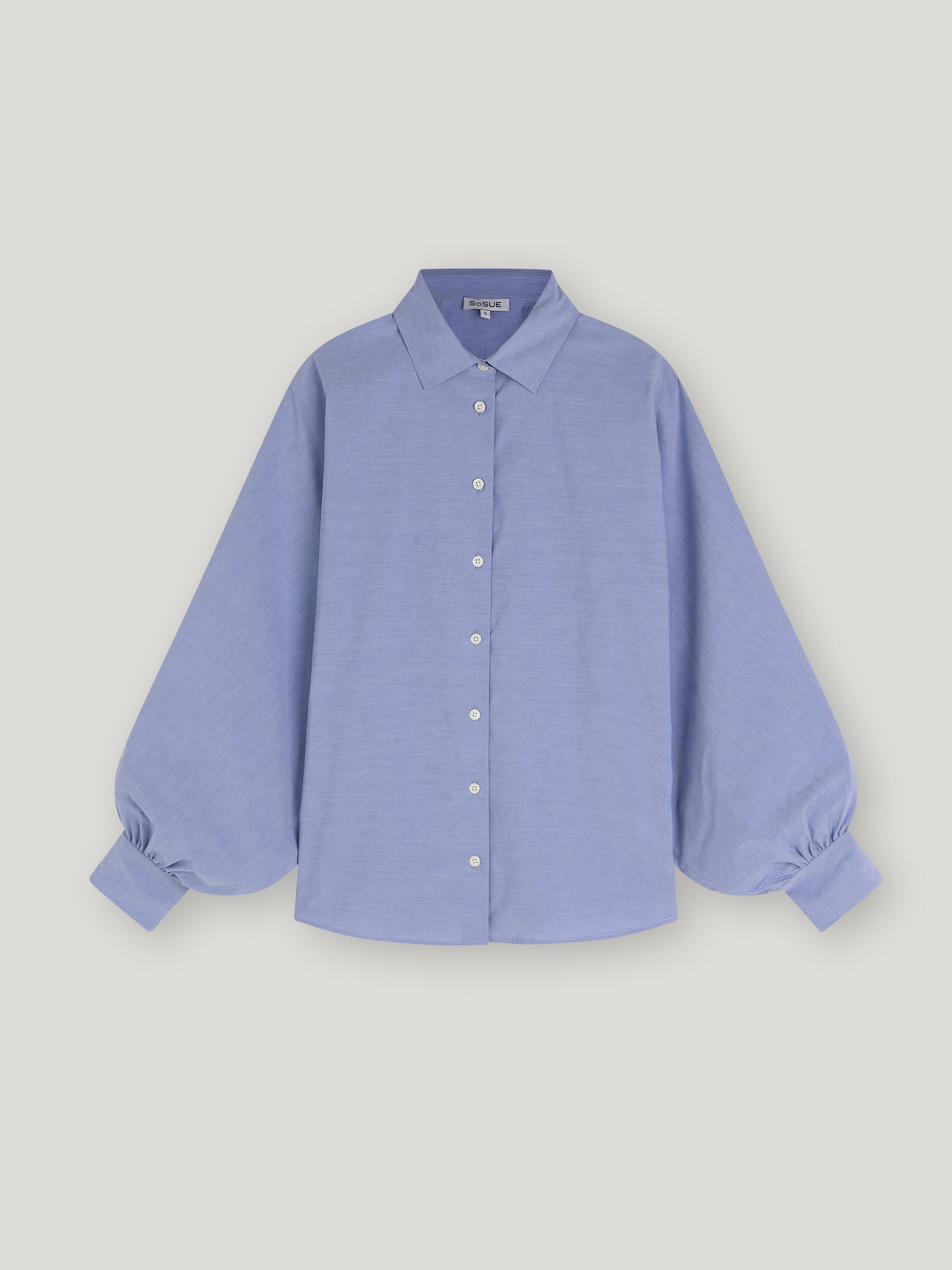 Bluse Antonia Slim Middleblue ist eine hellblaue Button-up-Bluse mit klassischem Kragen und langen, voluminösen Ballonärmeln, die an den Manschetten gerafft sind und so für einen Oversized-Look sorgen, auf einem schlichten weißen Hintergrund.