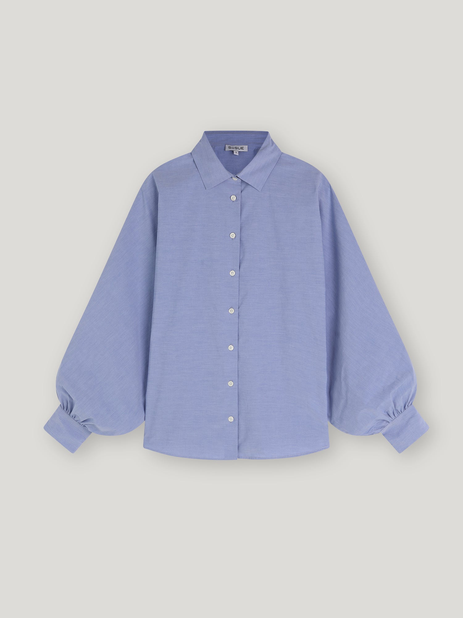 Bluse Antonia Slim Middleblue ist eine hellblaue Button-up-Bluse mit klassischem Kragen und langen, voluminösen Ballonärmeln, die an den Manschetten gerafft sind und so für einen Oversized-Look sorgen, auf einem schlichten weißen Hintergrund.