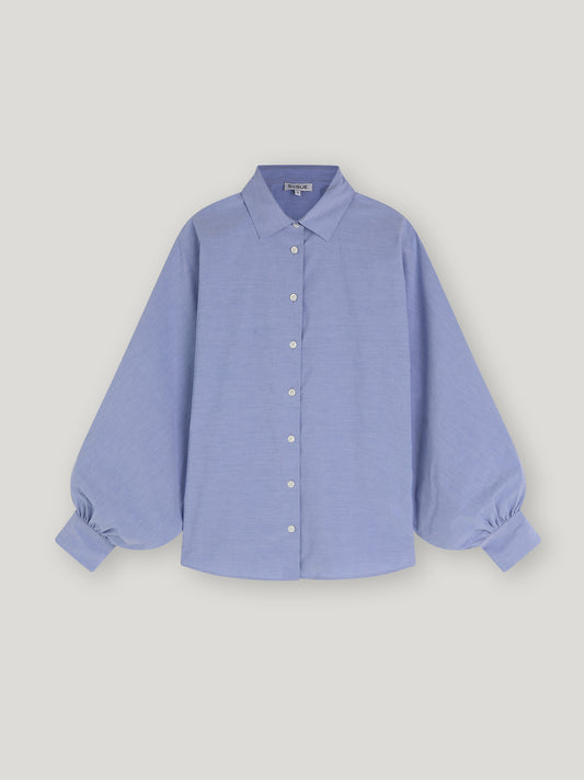 Bluse Antonia Slim Middleblue ist eine hellblaue Button-up-Bluse mit klassischem Kragen und langen, voluminösen Ballonärmeln, die an den Manschetten gerafft sind und so für einen Oversized-Look sorgen, auf einem schlichten weißen Hintergrund.