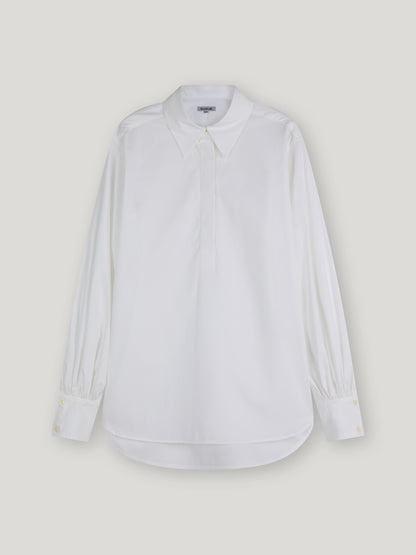 Die Bluse Rini White ist eine übergroße, langärmelige Popeline-Baumwollbluse mit spitzem Kragen und geknöpften Manschetten, die vor einem schlichten, hellen Hintergrund gezeigt wird.