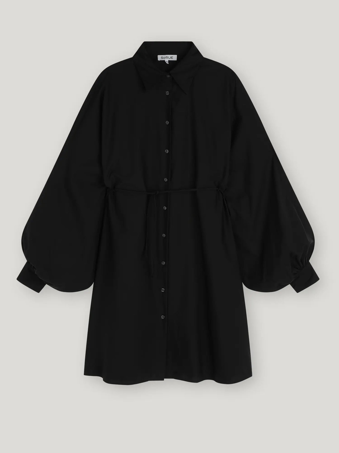 Das Dress Antonia Dress Vol. 2 Black ist ein schwarzes Damenkleid mit Kragen, langen Puffärmeln, Manschetten an den Handgelenken, Taillenband und Oversized-Schnitt, abgebildet auf einem hellgrauen Hintergrund.