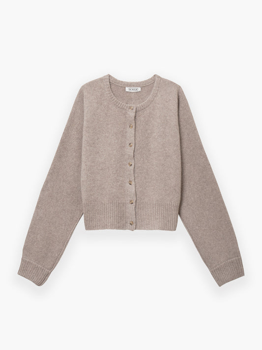 Die Jacke Cashmere Beige ist eine hellbeige, langärmelige, kurz geschnittene Strickjacke mit Rundhalsausschnitt und gerippten Bündchen und Saum, die flach auf weißem Grund liegt.