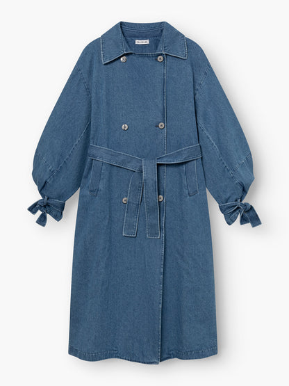 Der Antonia Denim Trench ist ein langer blauer Mantel mit Taillengürtel, doppelreihiger Knopfleiste, klassischem Kragen, sichtbaren Nahtdetails, an den Handgelenken gerafften Ärmeln mit geknüpften Manschetten und einfacher Einheitsgröße.