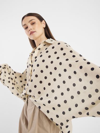 Eine Frau posiert mit erhobenen Armen, trägt die Bluse Antonia Dots Ecru Black und eine locker sitzende beigefarbene Hose und kreiert so einen stilvollen Sommerlook Damen vor einem schlichten weißen Hintergrund.