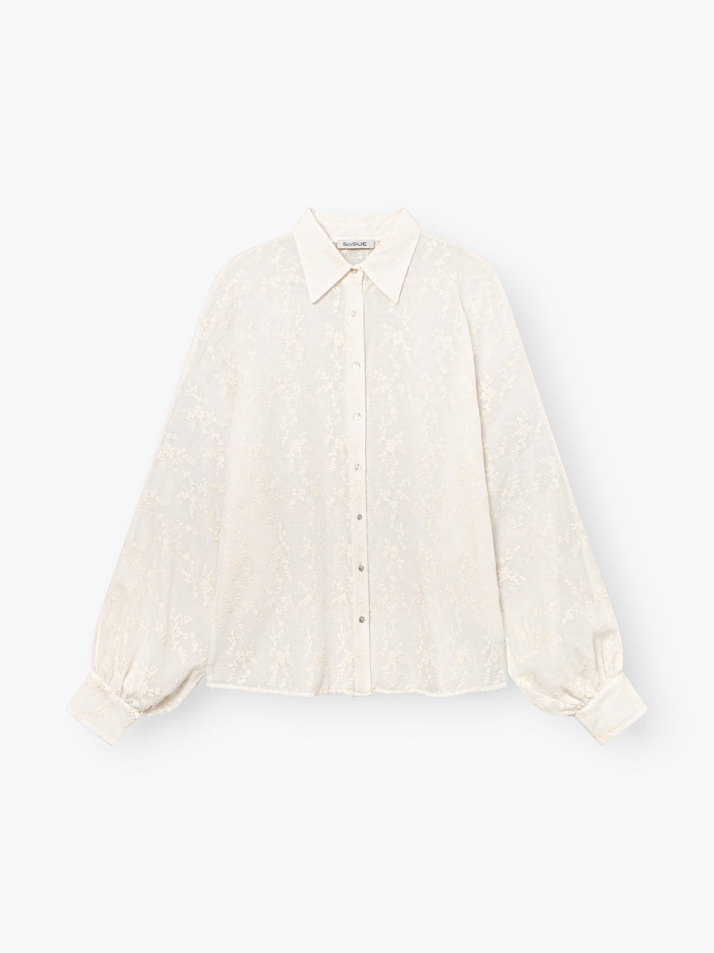 Die Bluse Antonia Embrodery Creme ist eine cremefarbene, langärmelige Bluse mit dezentem Blumenmuster, spitzem Kragen, geknöpfter Vorderseite und breiten Manschetten, abgebildet auf weißem Grund.
