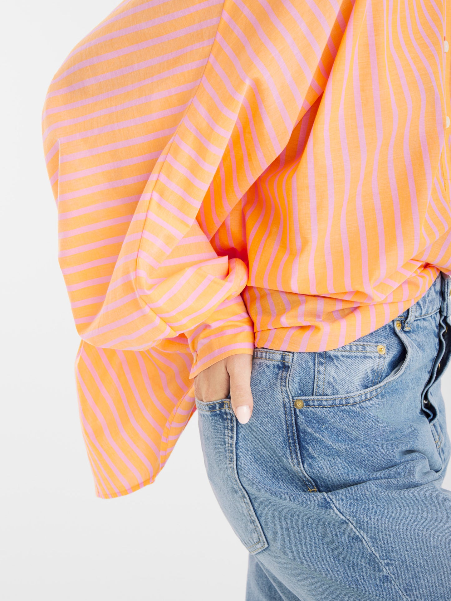 Eine Person trägt das Antonia-Voile-Hemd in Korallenrosa, locker sitzend und mit einer Hand in der Hosentasche vor einem einfarbig weißen Hintergrund, in eine hochgezogene Bluejeans gesteckt.