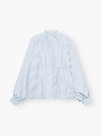 Die Bluse Antonia Smoking Blue Stripes hat hellblaue und weiße Streifen, lange Puffärmel, einen hohen Kragen, Falten im Smoking-Stil und eine geknöpfte Vorderseite, die auf weißem Hintergrund gezeigt wird.