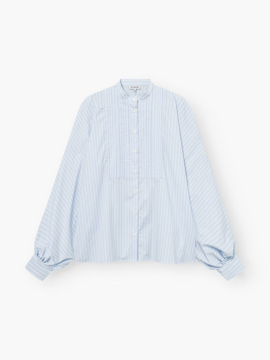 Die Bluse Antonia Smoking Blue Stripes hat hellblaue und weiße Streifen, lange Puffärmel, einen hohen Kragen, Falten im Smoking-Stil und eine geknöpfte Vorderseite, die auf weißem Hintergrund gezeigt wird.