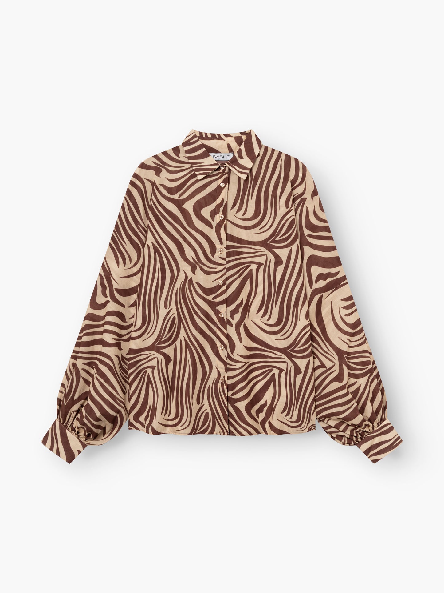 Die Antonia Voile Zebra Brown ist eine langärmelige Bluse mit braunem und beigem Zebramuster, Kragen und gerafften Manschetten. Die in Italien gefertigte Bluse besticht durch ihren Stil und ihre hochwertige Verarbeitung und wird flach auf weißem Grund gezeigt.