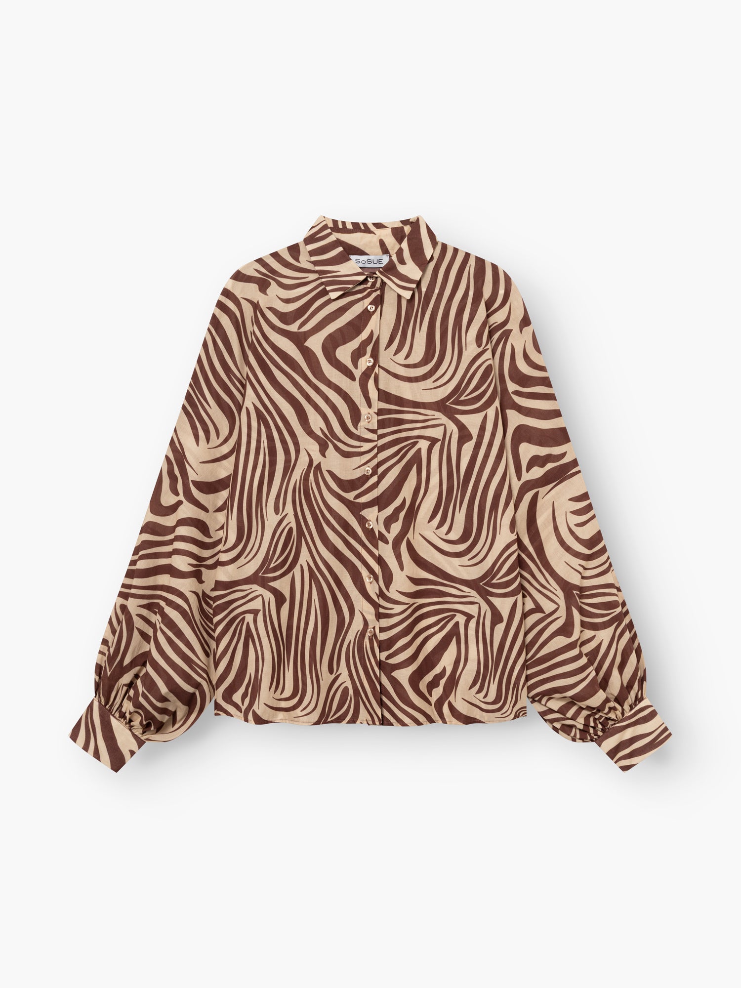Die Antonia Voile Zebra Brown ist eine langärmelige Bluse mit braunem und beigem Zebramuster, Kragen und gerafften Manschetten. Die in Italien gefertigte Bluse besticht durch ihren Stil und ihre hochwertige Verarbeitung und wird flach auf weißem Grund gezeigt.
