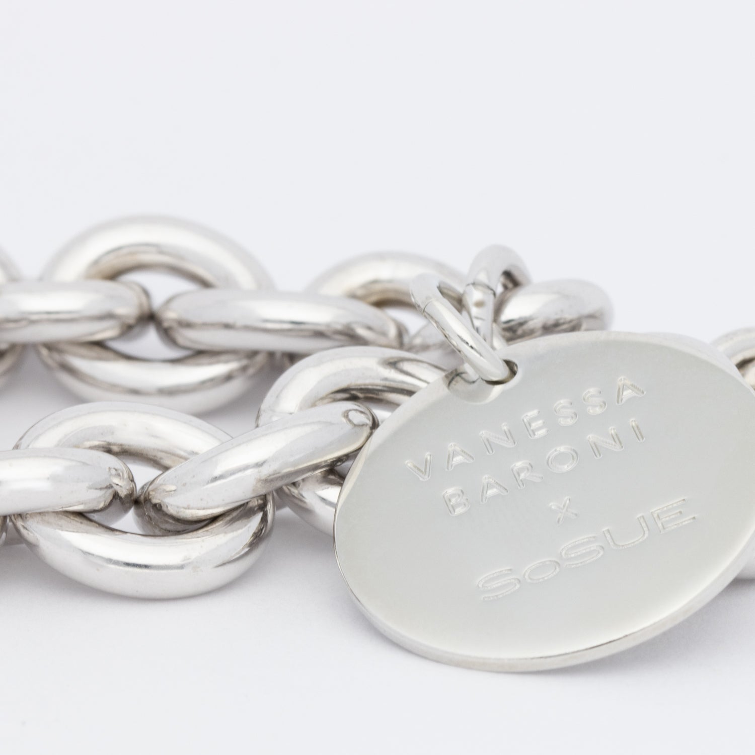 Eine Nahaufnahme des Vanessa Baroni x SOSUE Armbands Silber, ein klobiges silbernes Damenarmband mit einem runden, flachen Anhänger, auf dem VANESSA BARONI x SoSUE eingraviert ist, vor einem schlichten weißen Hintergrund.