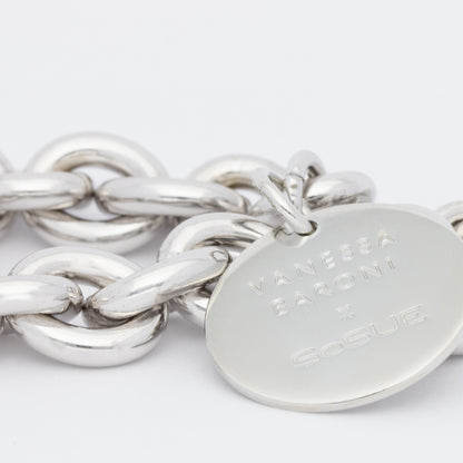 Eine Nahaufnahme des Vanessa Baroni x SOSUE Armbands Silber, ein klobiges silbernes Damenarmband mit einem runden, flachen Anhänger, auf dem VANESSA BARONI x SoSUE eingraviert ist, vor einem schlichten weißen Hintergrund.