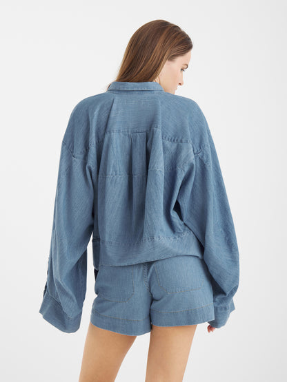 Eine Frau mit langen Haaren steht in einer locker sitzenden Jeansjacke und Shorts Dark Denim vor einem schlichten weißen Hintergrund.