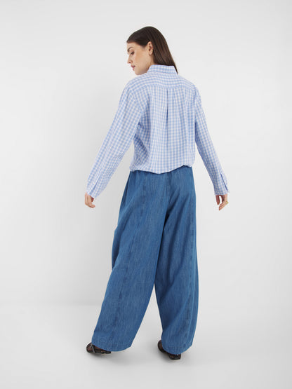 Eine Frau mit glattem, offenem Haar steht vor einem schlichten weißen Hintergrund und trägt das langärmelige Hemd Blouse Casual Check Blue White Check und eine weit geschnittene Blue Jeans.