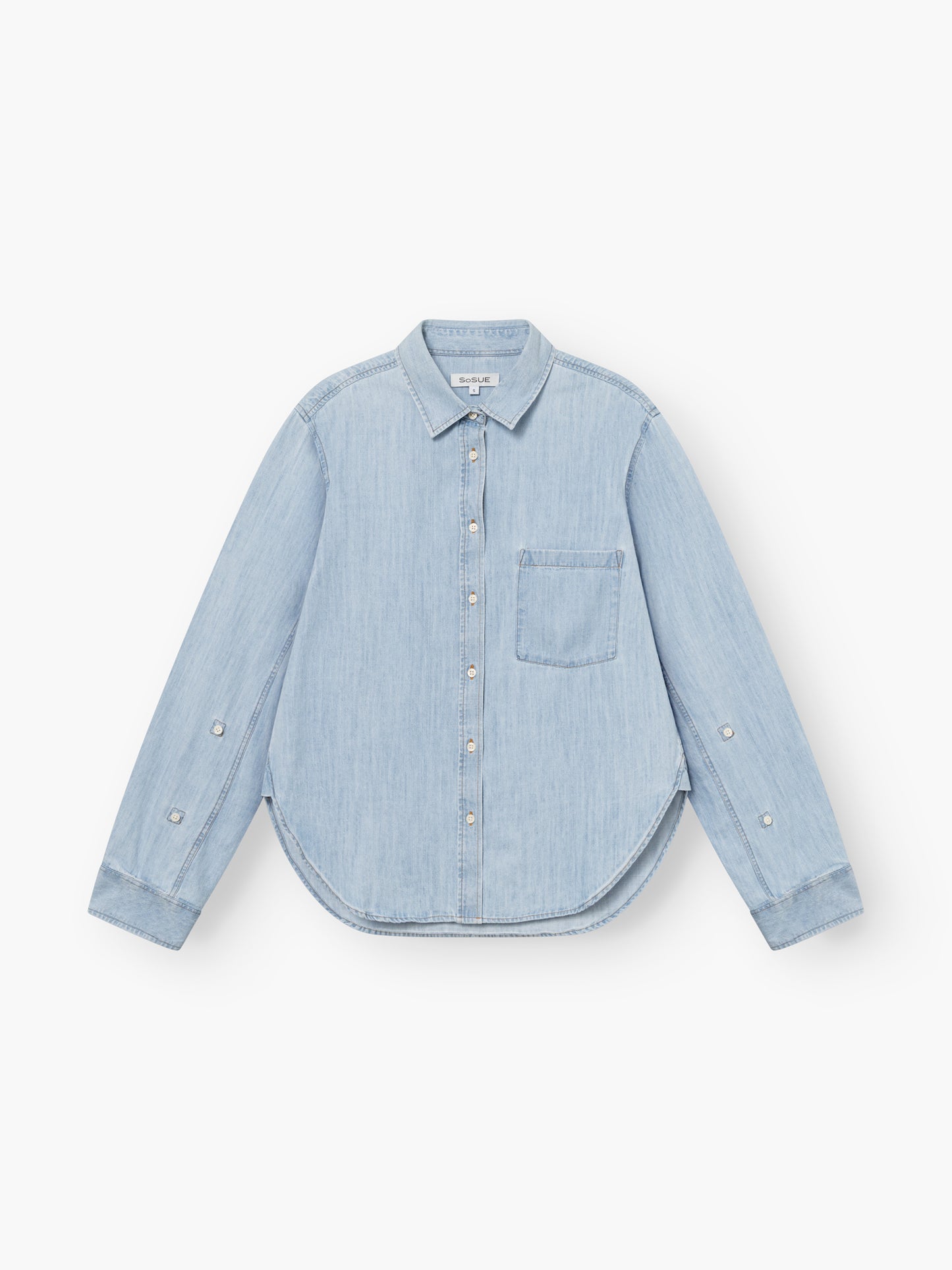 Bluse Classic Denim in Hellblau mit langen Ärmeln, einer Brusttasche, tailliertem Schnitt und geschwungenem Saum, flach auf weißem Grund gelegt.