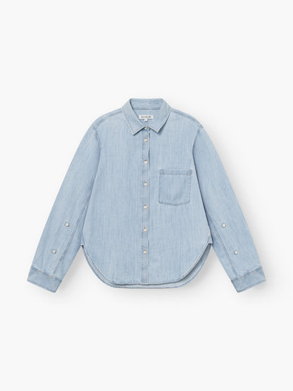 Bluse Classic Denim in Hellblau mit langen Ärmeln, einer Brusttasche, tailliertem Schnitt und geschwungenem Saum, flach auf weißem Grund gelegt.