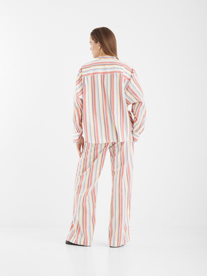 Eine Frau blickt von sich weg, sie trägt die Pants New York - einen locker sitzenden Schlafanzug mit vertikalen pastellfarbenen Streifen in Rosa, Gelb, Blau und Weiß - vor einem schlichten weißen Hintergrund.