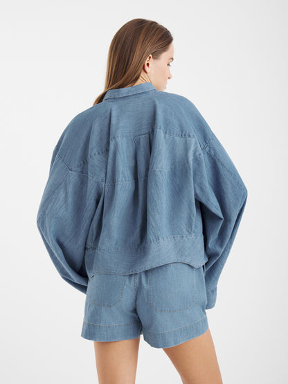 Eine Frau mit langen braunen Haaren, von hinten gesehen, trägt die Blouse Bomber Denim Jacke und dazu passende Jeansshorts vor einem schlichten weißen Hintergrund.