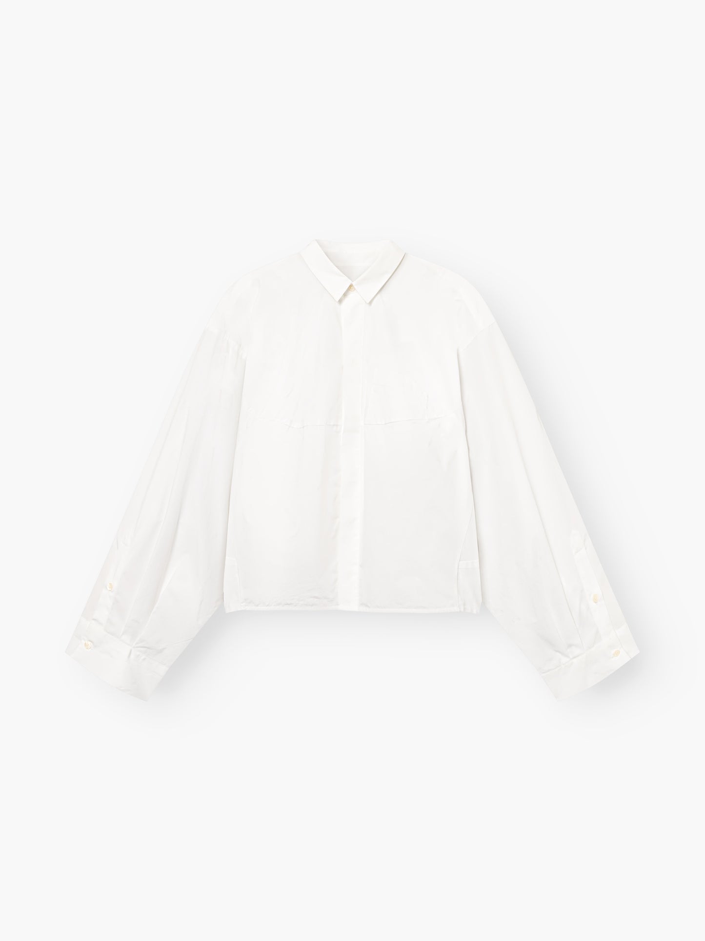 Die Blouse Bomber White ist eine weiße, langärmelige Button-up-Bluse mit Kragen und weiten, leicht gepufften Ärmeln, die vor einem einfarbig weißen Hintergrund gezeigt wird.