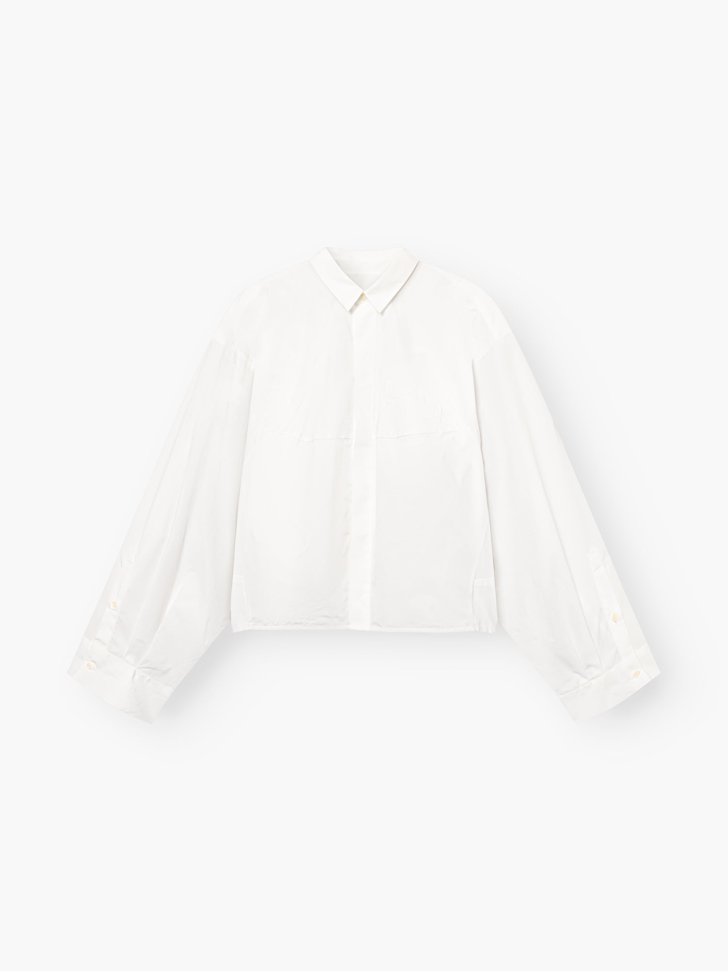 Die Blouse Bomber White ist eine weiße, langärmelige Button-up-Bluse mit Kragen und weiten, leicht gepufften Ärmeln, die vor einem einfarbig weißen Hintergrund gezeigt wird.
