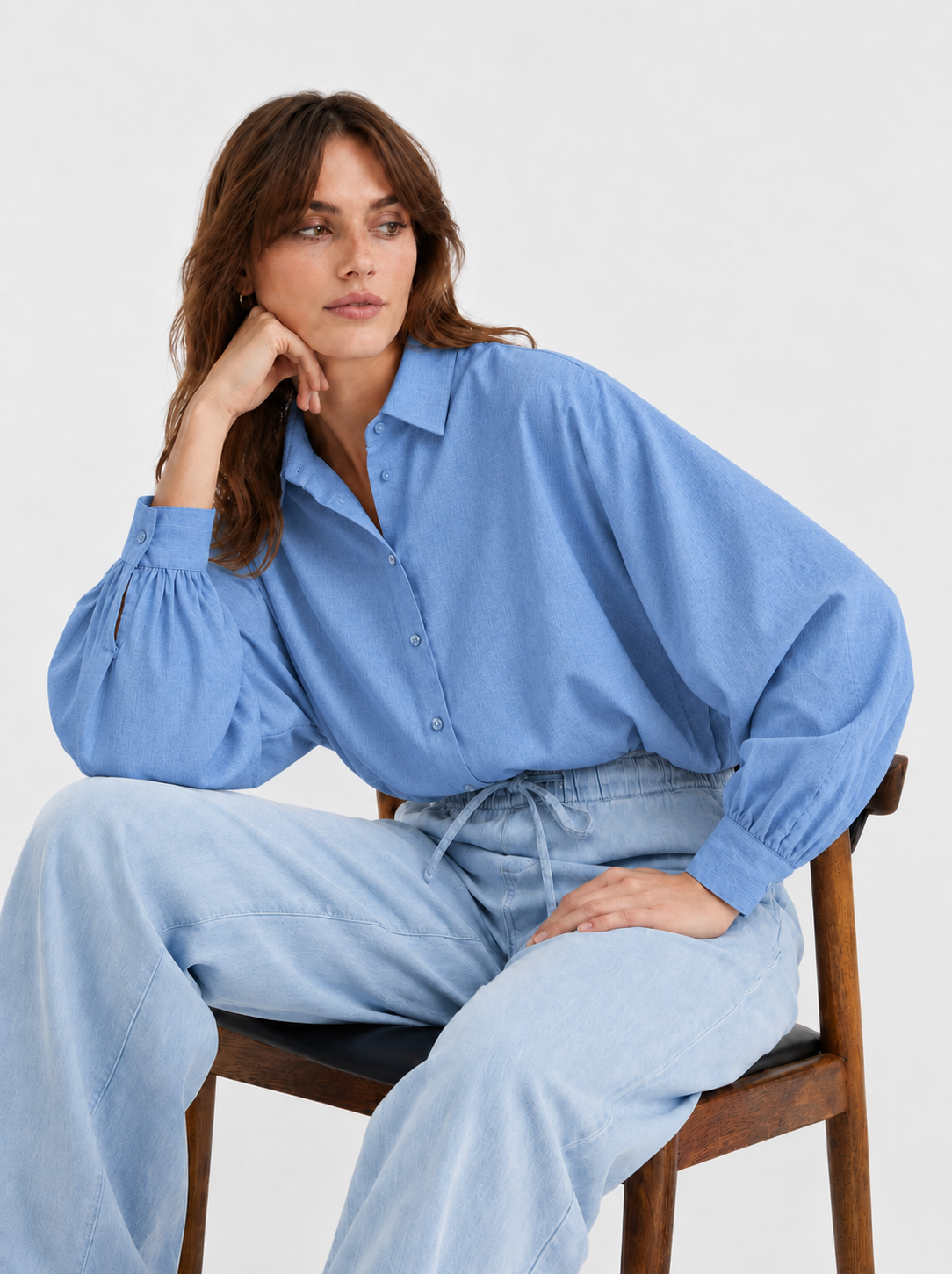 Eine Frau sitzt auf einem Holzstuhl und trägt ein Baumwollflanellhemd Bluse Antonia Slim Flanell Light Blue sowie eine locker sitzende Jeans.