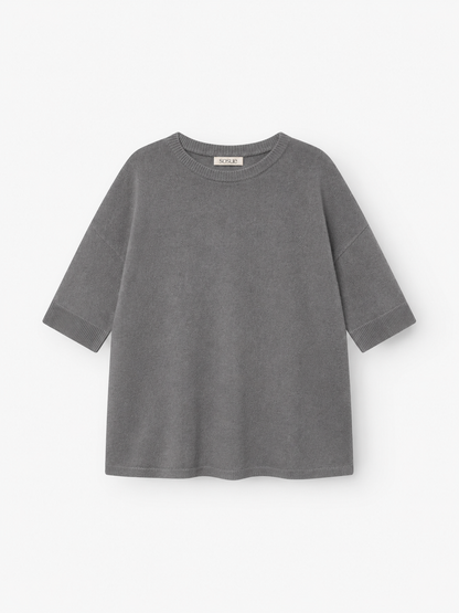 Ein graues Strick-T-Shirt „Aurora Anthra“ mit kurzen Ärmeln, lockerer Passform und rundem Ausschnitt, gefertigt aus weichem Strickstoff und flach auf weißem Hintergrund präsentiert.