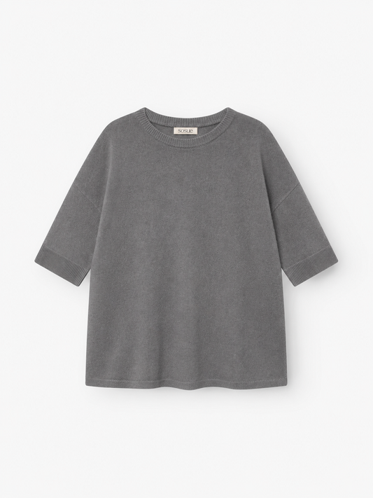 Ein graues Strick-T-Shirt „Aurora Anthra“ mit kurzen Ärmeln, lockerer Passform und rundem Ausschnitt, gefertigt aus weichem Strickstoff und flach auf weißem Hintergrund präsentiert.