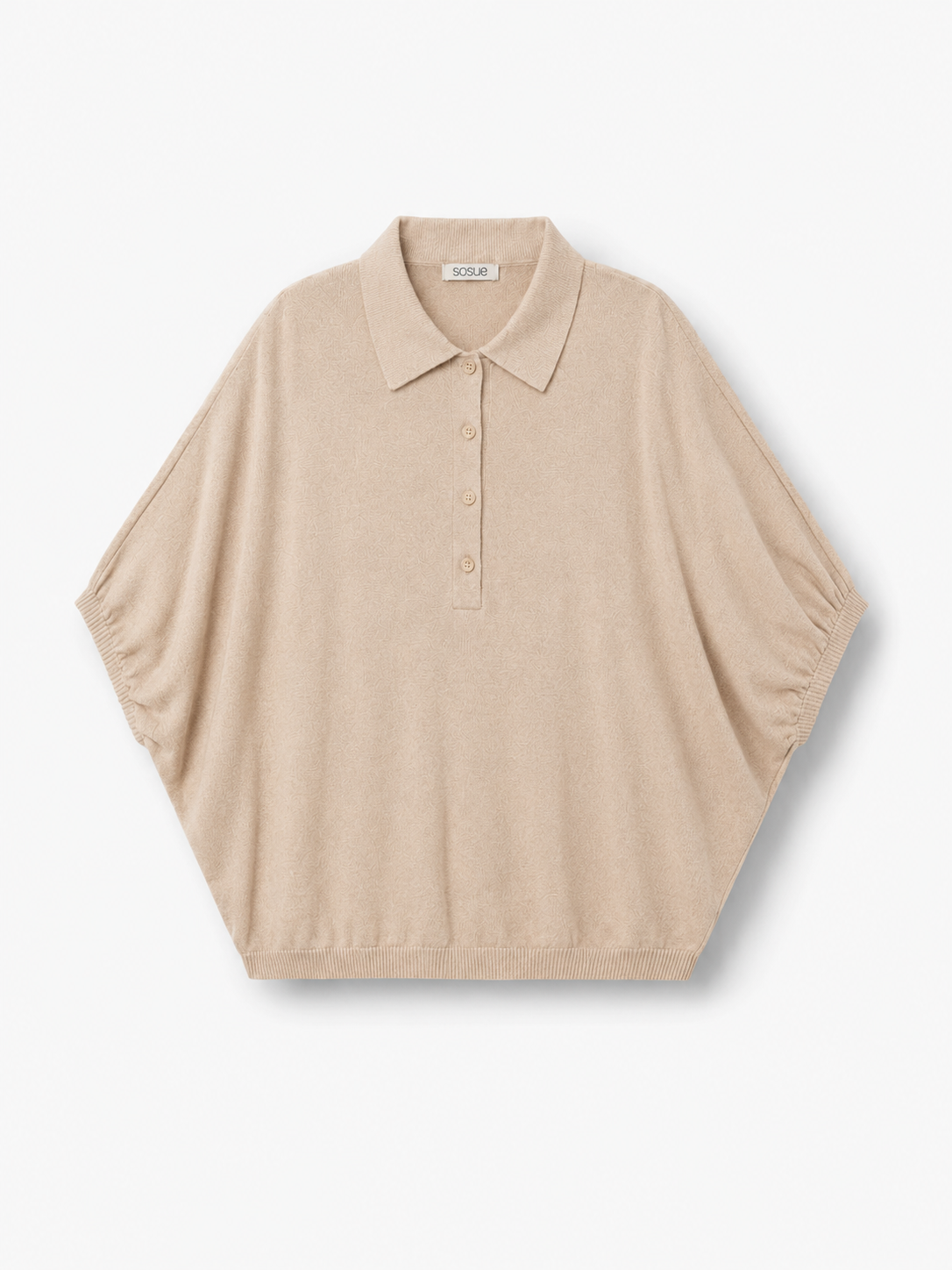 Cowboy Polo Knit Powder: Ein kurzärmeliges, locker sitzendes Strickoberteil in Puderbeige mit Polokragen und Knopfleiste, abgebildet vor einem schlichten weißen Hintergrund.