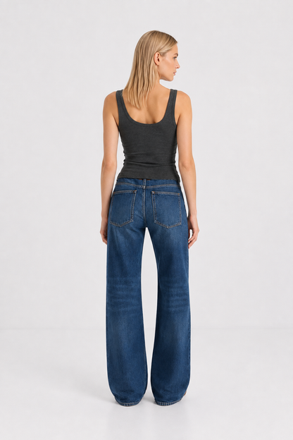 Eine Frau steht mit dem Rücken zur Kamera und trägt das figurbetonte Tanktop „Anthrazit“ sowie eine hoch taillierte Bluejeans mit weitem Bein. Sie hat glattes blondes Haar und posiert vor einem schlichten weißen Hintergrund.