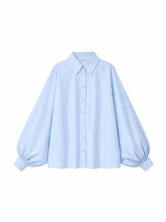 Die Bluse „Antonia Hellblau“ aus Baumwolle ist eine hellblaue Bluse mit Knopfleiste, langen, voluminösen Ballonärmeln, einem spitzen Kragen und breiten Manschetten. Diese elegante hellblaue Baumwollbluse in Einheitsgröße wird vor einem weißen Hintergrund gezeigt.