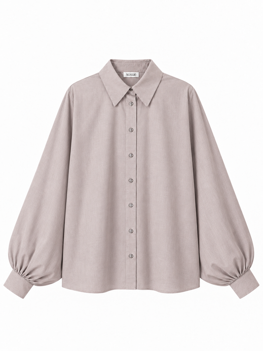 Die Bluse „Antonia Flanell Light Taupe“ ist eine elegante, langärmelige Bluse in hellem Taupe mit spitzem Kragen, Knopfleiste vorne und weit fallenden Ärmeln, die an den Manschetten gerafft sind. Diese in Portugal hergestellte Oversize-Damenbluse wird vor einem weißen Hintergrund präsentiert.