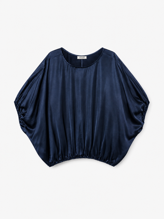 Die „Bluse Cowboy Shiny Navy“ ist eine marineblaue, kurzärmelige Damenbluse aus Satin mit lockerer, drapierter Passform und elastischem Saum. Diese Oversize-Bluse verfügt über einen abgerundeten, weiten Ausschnitt und besticht durch eine glänzende, glatte Oberfläche, die für einen mühelos eleganten Look sorgt.