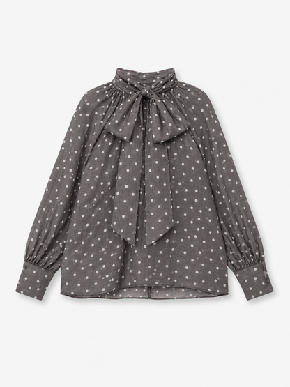 Eine langärmelige graue Bluse „Dotty Bow Grey Latte“ aus Baumwoll-Voile mit weißen Polka-Punkten, die sich durch einen hohen Kragen und eine große Schleife am Kragen auszeichnet. Diese elegante Bluse wird in Italien meisterhaft gefertigt und vereint klassischen Charme mit hochwertiger Handwerkskunst.