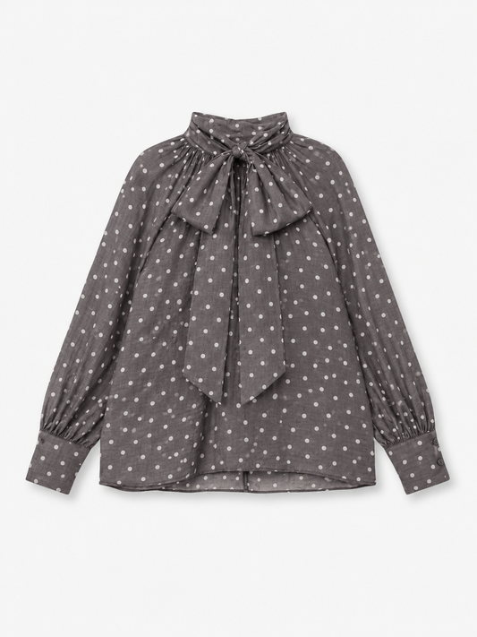 Eine langärmelige graue Bluse „Dotty Bow Grey Latte“ aus Baumwoll-Voile mit weißen Polka-Punkten, die sich durch einen hohen Kragen und eine große Schleife am Kragen auszeichnet. Diese elegante Bluse wird in Italien meisterhaft gefertigt und vereint klassischen Charme mit hochwertiger Handwerkskunst.