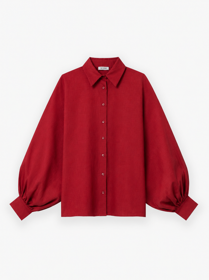 Die Bluse „Antonia Burgundy“ ist eine Damenbluse in einem satten Burgunderrot mit langen Ärmeln, einer Knopfleiste vorne und einem klassischen Kragen. Dieses elegante Modell mit voluminösen Puffärmeln aus weichem Baumwoll-Voile wird vor einem weißen Hintergrund präsentiert.