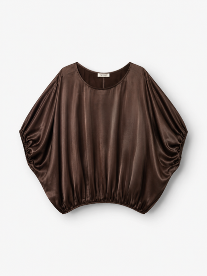 Die Bluse „Cowboy Shiny Braun“ in Dunkelbraun mit glänzender Oberfläche und Fledermausärmeln ist aus LENZING™ ECOVERO™-Viskose gefertigt und verleiht einen eleganten Touch. Diese locker sitzende Damenbluse, hergestellt in Portugal, verfügt über einen gerafften Saum und kommt vor weißem Hintergrund besonders gut zur Geltung.